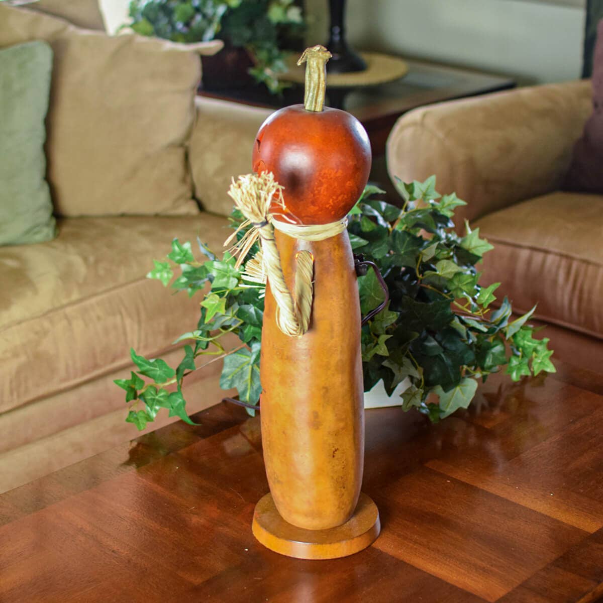 A decorative carved gourd with a reddish-brown pumpkin top displayed on a wooden table in a living room setting.