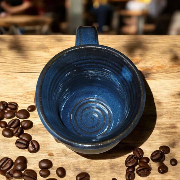 Blue ceramic mug on a wooden table with coffee beans around it