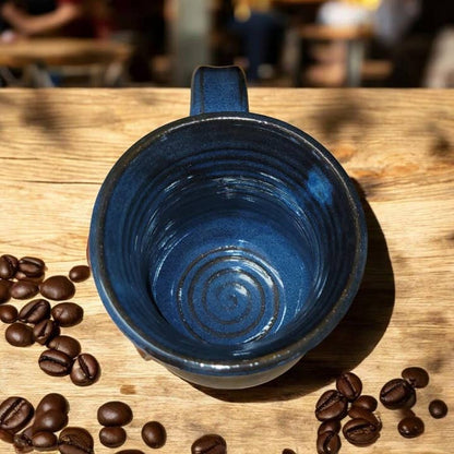 Blue ceramic mug on a wooden table with coffee beans around it