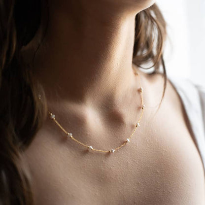 Close-up of a person wearing a delicate gold necklace with small pearls.