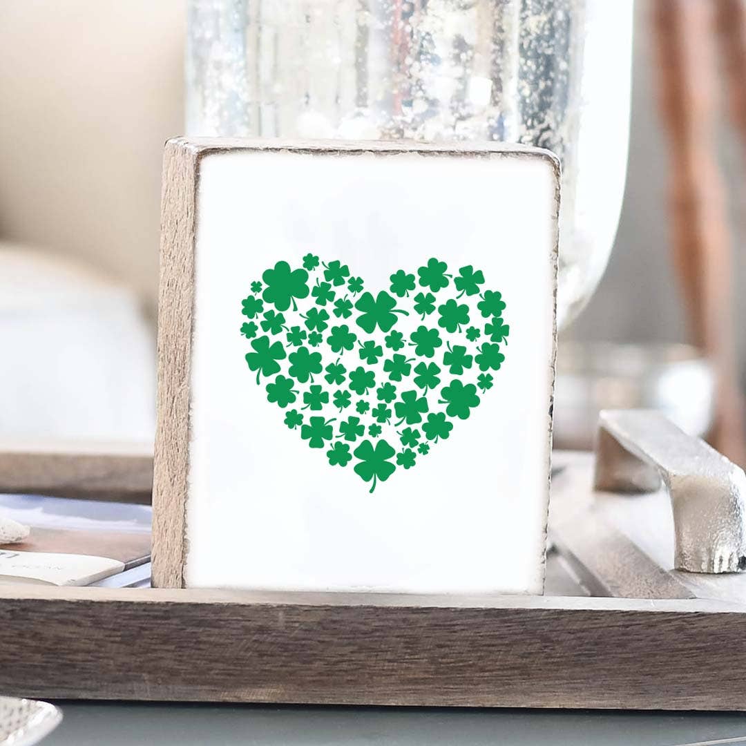 Heart-shaped design made of green shamrocks on a white background in a wooden frame.