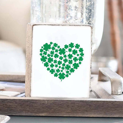 Heart-shaped design made of green shamrocks on a white background in a wooden frame.