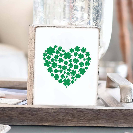 Heart-shaped design made of green shamrocks on a white background in a wooden frame.