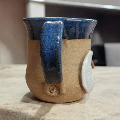 Ceramic mug with blue handle and beige body on a wooden surface