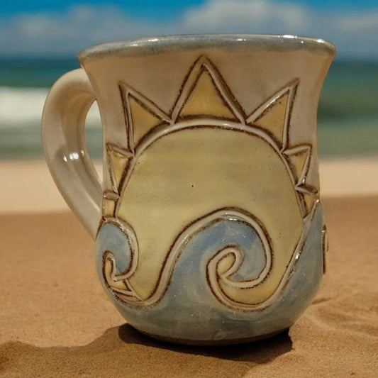 Ceramic mug with sun and wave design on a sandy beach
