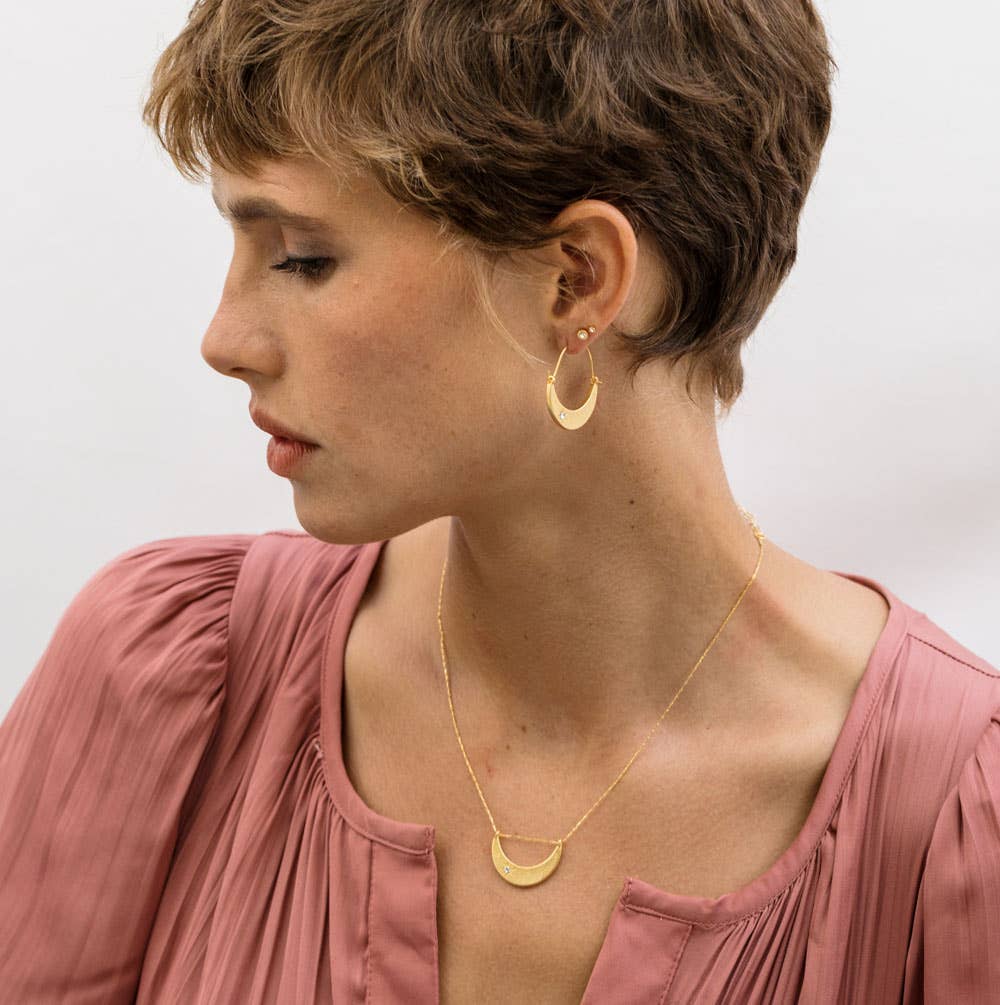 Woman wearing gold hoop earrings and a necklace with a plain background