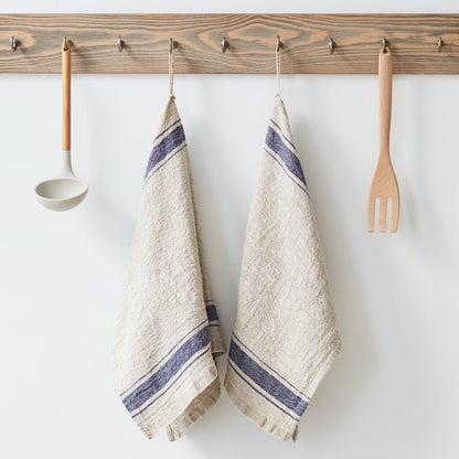 Two beige towels with blue stripes hanging on a wooden rack with kitchen utensils.
