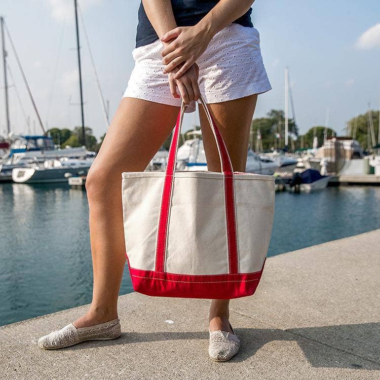 Person holding a red and white tote bag by a marina