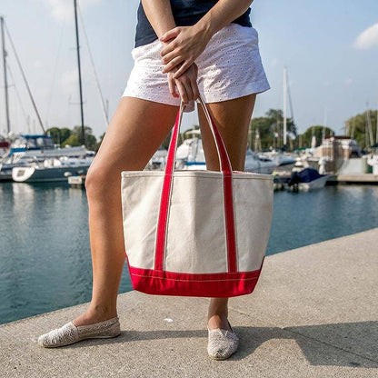 Person holding a red and white tote bag by a marina