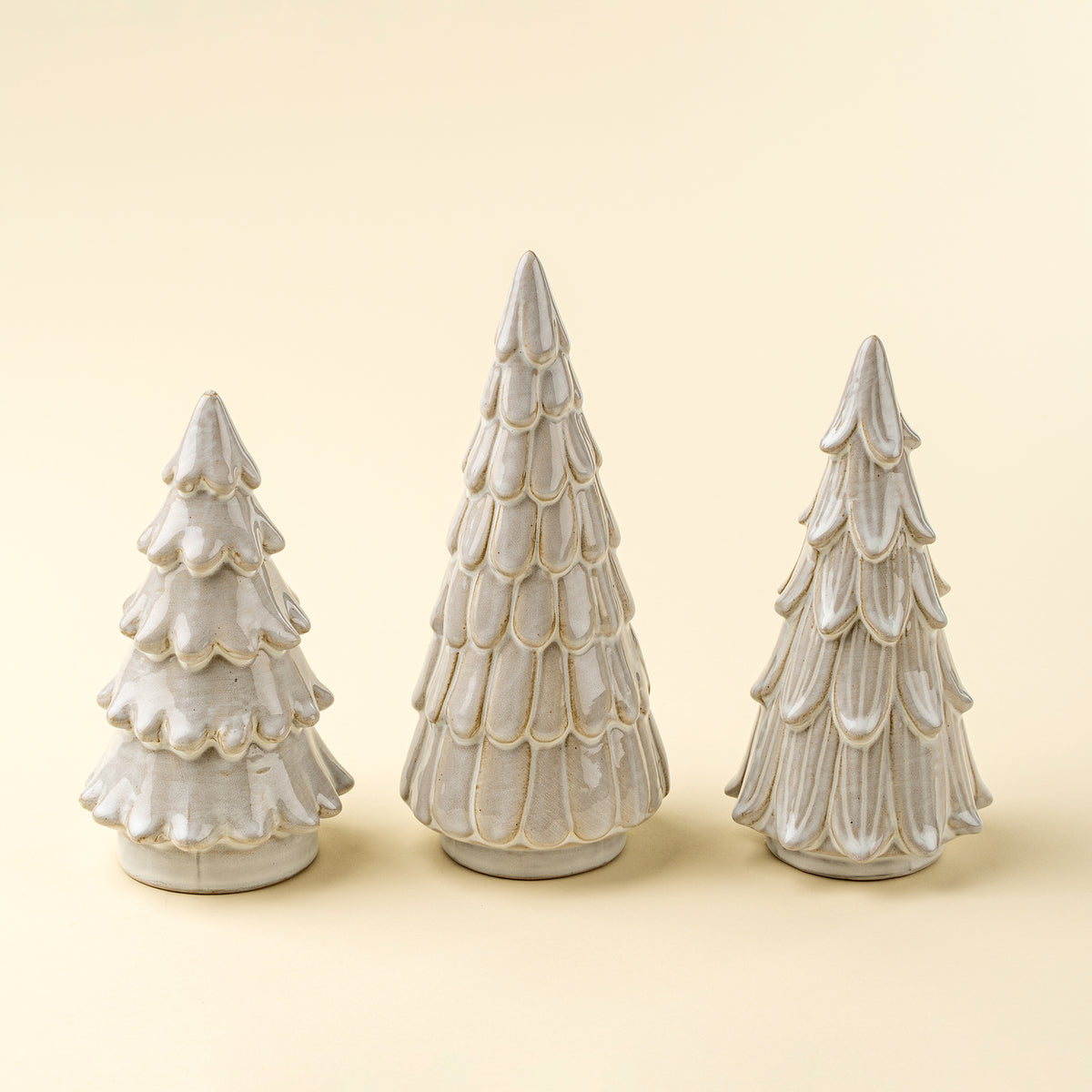 Three decorative ceramic Christmas trees with scalloped edges on a beige background