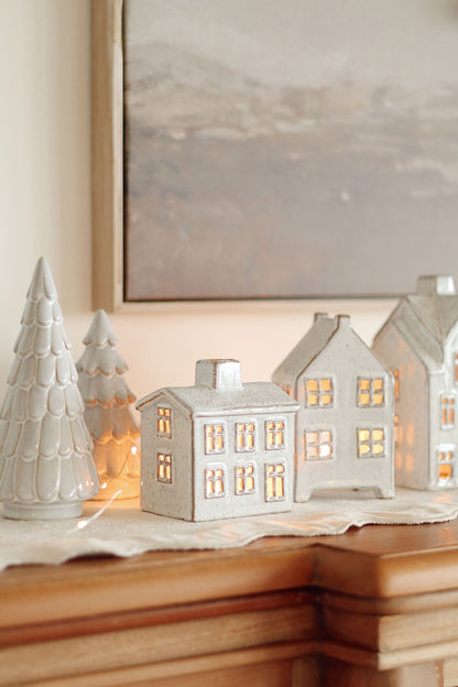 Set of ceramic house-shaped lanterns with glowing lights and ceramic trees on a surface.
