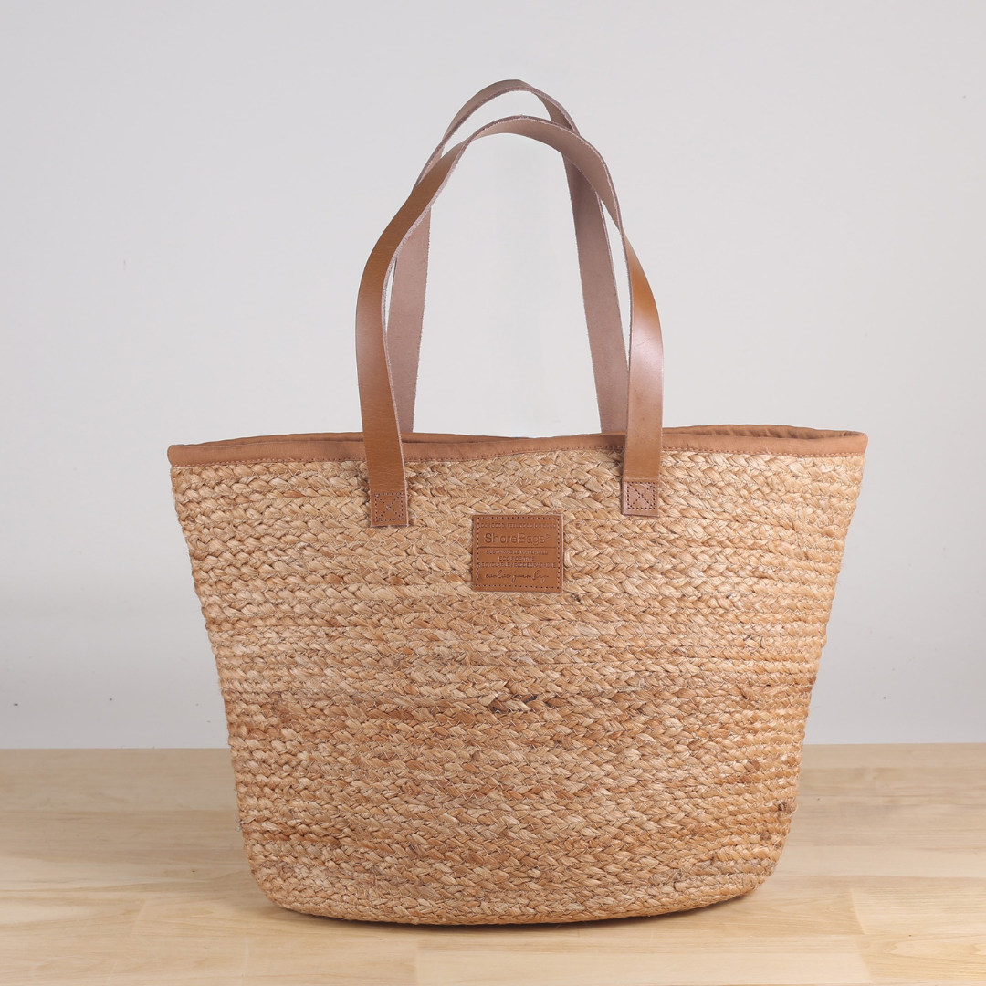 Woven tote bag with brown leather handles on a wooden surface