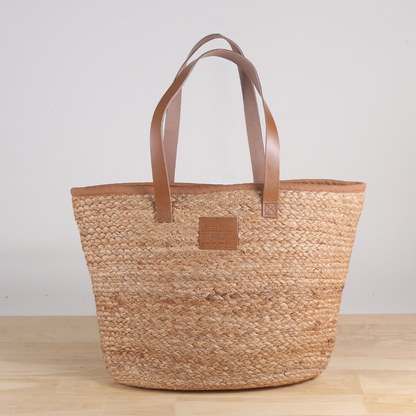 Woven tote bag with brown leather handles on a wooden surface
