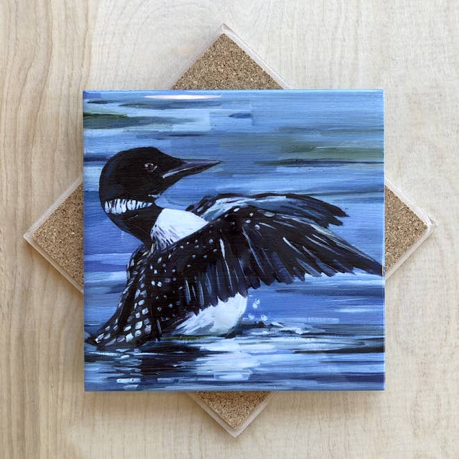 Trivet with a painting of a loon on water, placed on a wooden surface.