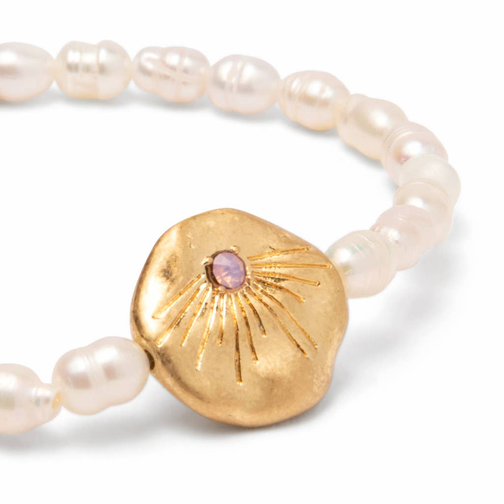 Pearl bracelet with a gold disc featuring a pink stone on a white background