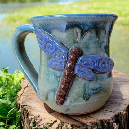Ceramic mug with dragonfly design on a tree stump outside