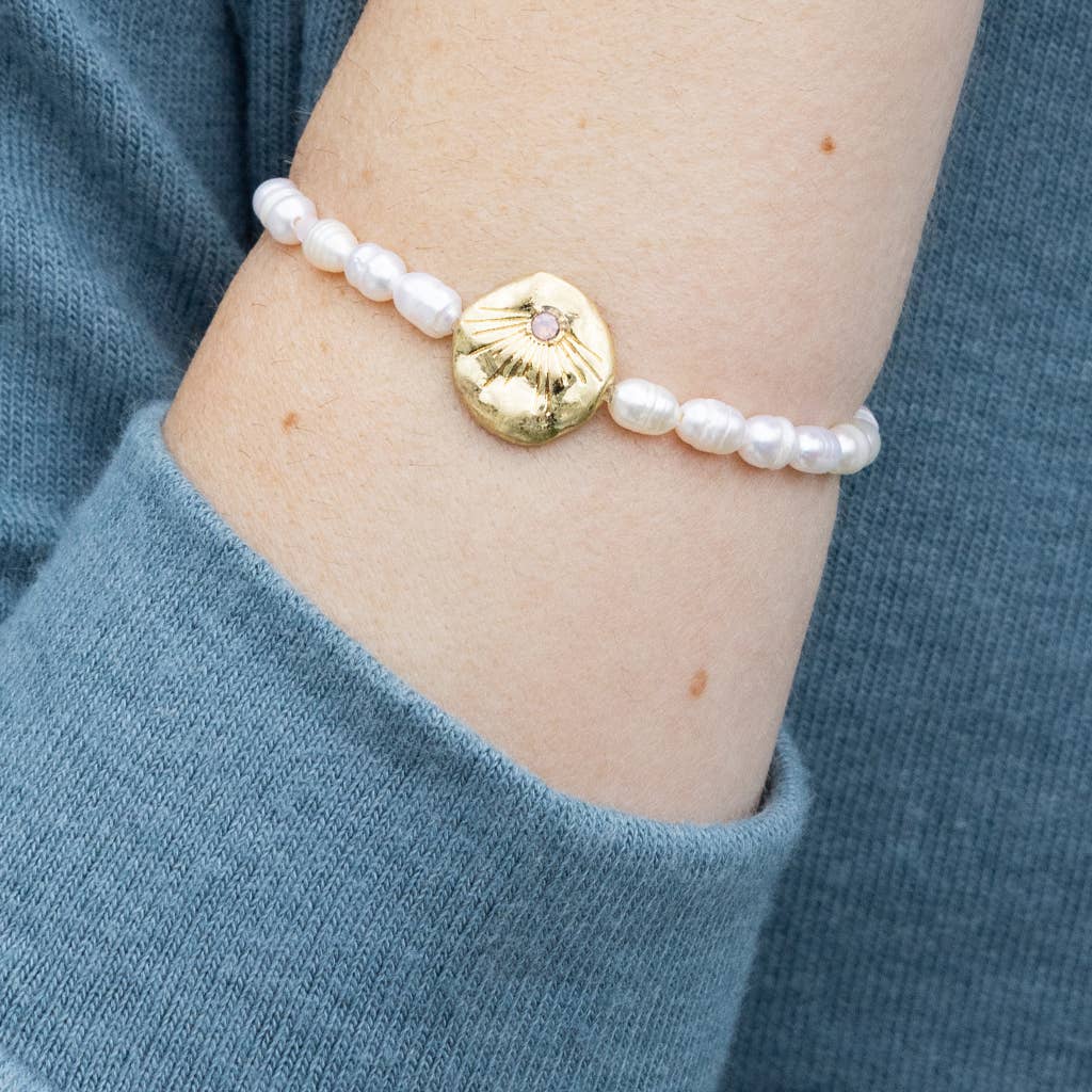 Pearl bracelet with a gold disc on a wrist, against a blue sleeve background