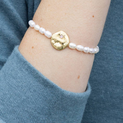 Pearl bracelet with a gold disc on a wrist, against a blue sleeve background