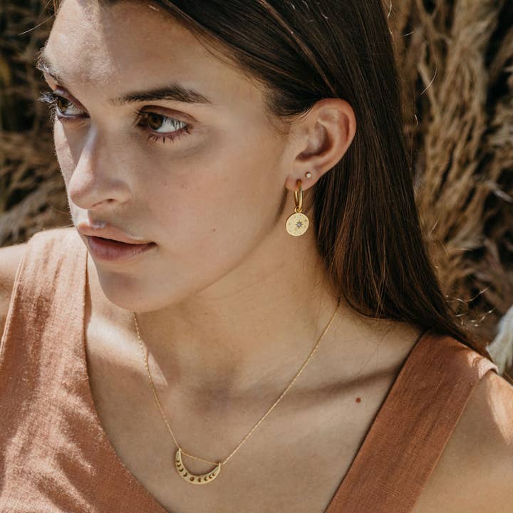 Woman wearing gold earrings and a necklace with a natural background
