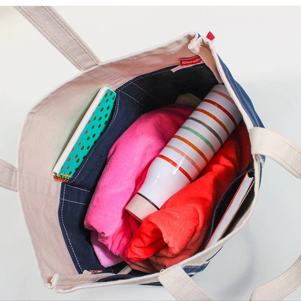 Open tote bag with colorful clothes and a striped water bottle inside, on a light background