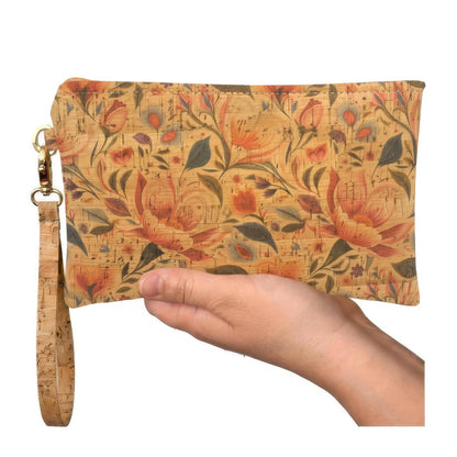 A rectangular clutch purse with a floral and botanical pattern in orange, red, green, and beige, held in a hand. The clutch has a cork-look wrist strap and gold-tone hardware.