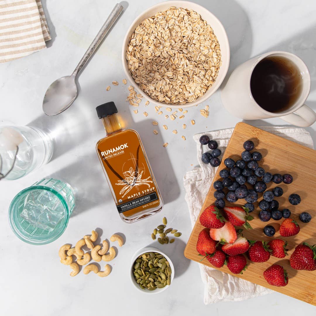 Tabletop scene with Runamok maple syrup bottle, fruits, nuts, and a bowl of oats.