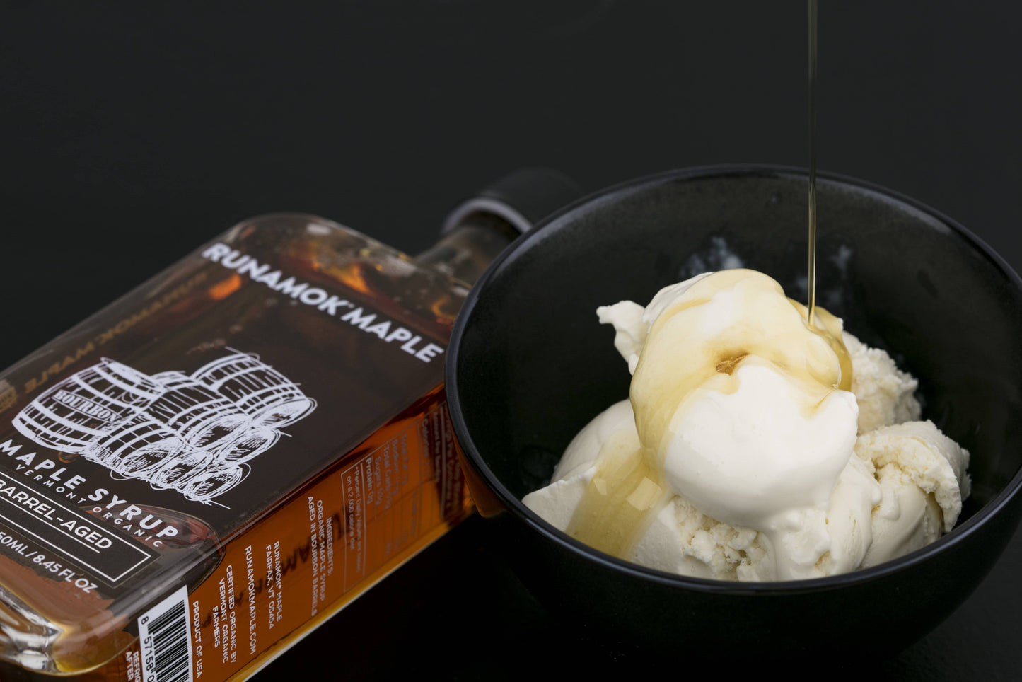 Bowl of ice cream with maple syrup being poured over it, next to a bottle of Runamok Maple syrup.