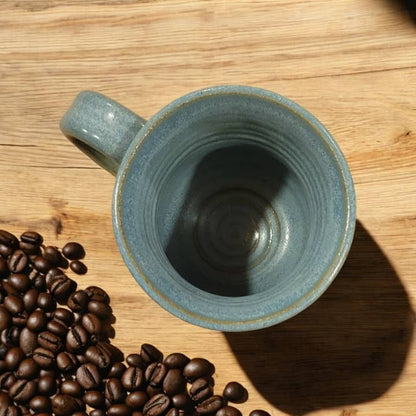 Blue ceramic mug on a wooden surface with coffee beans
