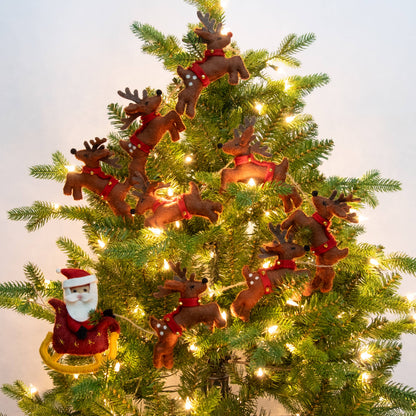 A decorated Christmas tree with garland of brown reindeer and a Santa Claus in a sleigh, lit by warm white string lights against a pale background.