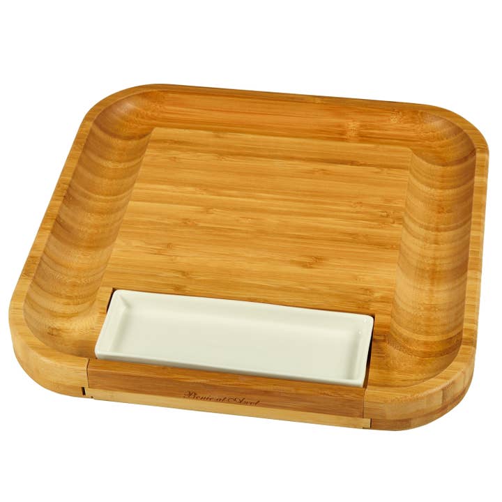 Wooden charcuterie board with a white rectangular dish inside on a white background