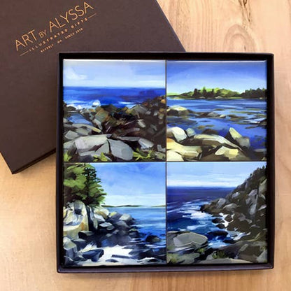 Set of four coastal landscape coasters in a gift box on a wooden surface with 'Art by Alyssa' branding.