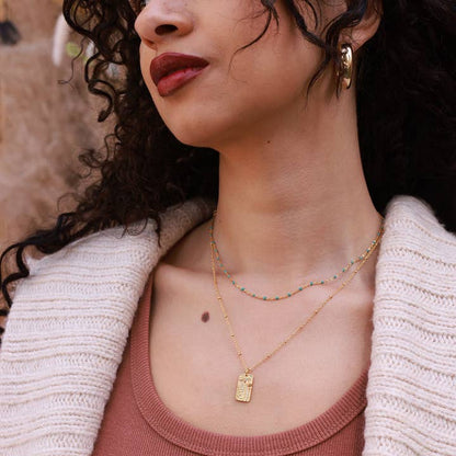 Woman wearing gold necklaces and earrings with a neutral background