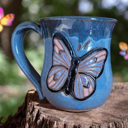 Blue ceramic mug with a butterfly design on a wooden surface with blurred butterfly wings in the background.