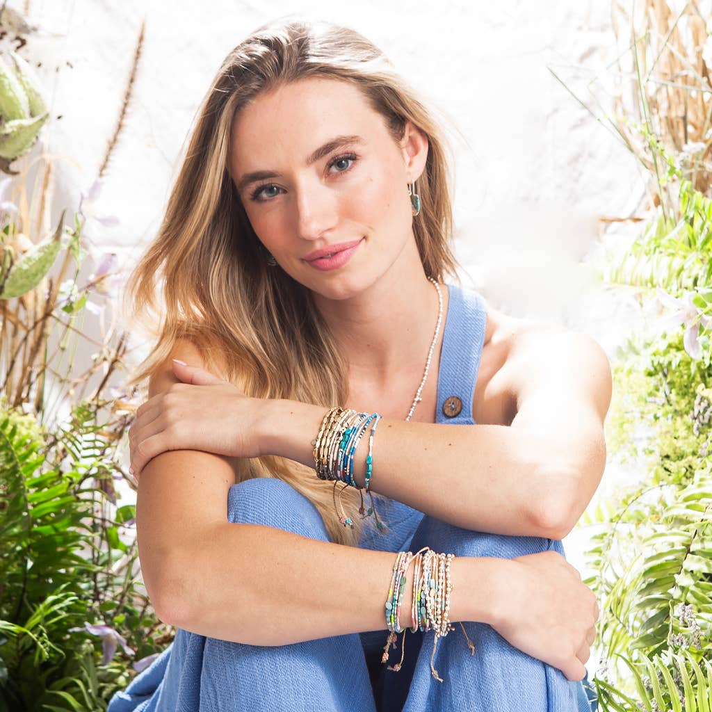 Woman in a blue dress and bracelets with greenery in the background