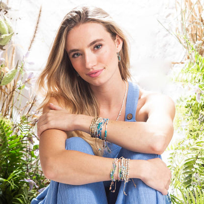 Woman in a blue dress and bracelets with greenery in the background