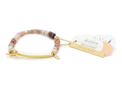 Bracelet with multicolored beads and gold bar, accompanied by a tag on a white background