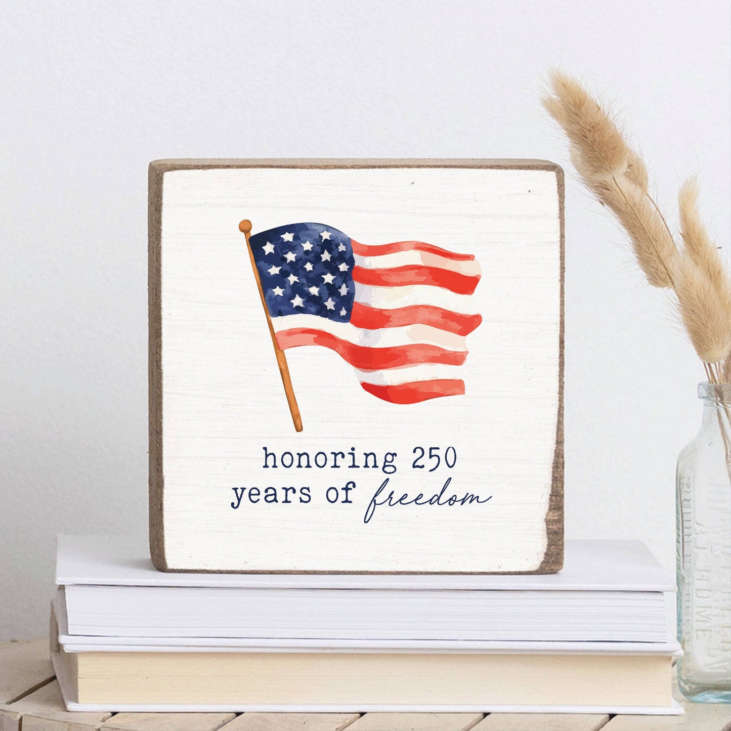 Decorative sign with American flag and text 'honoring 250 years of freedom' on a stack of books.