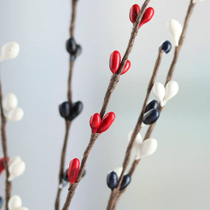 Close up of a decorative branch with red, blue, and white berries on a white background