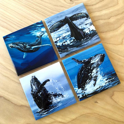 Four square coasters with whale designs on a wooden surface