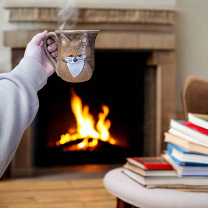 Person holding a mug with a fox design in front of a fireplace with books on a table.