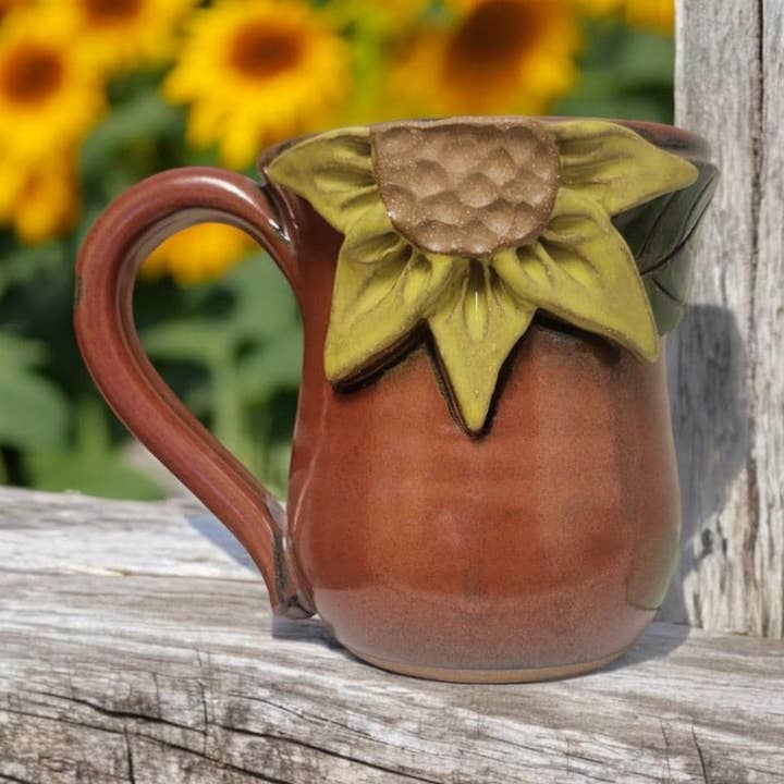 Ceramic mug with sunflower design on a wooden surface with sunflowers in the background