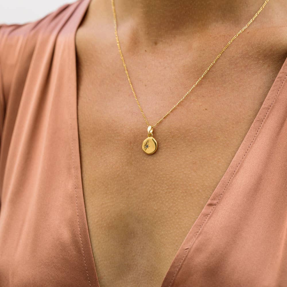 Gold necklace with a pendant on a person wearing a pink top.