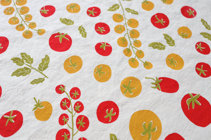 Close up of a white kitchen tea towel with a colorful print of red and yellow tomatoes and green leaves.