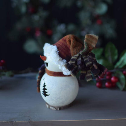 Decorative snowman figurine with a hat and scarf against a blurred Christmas tree background.
