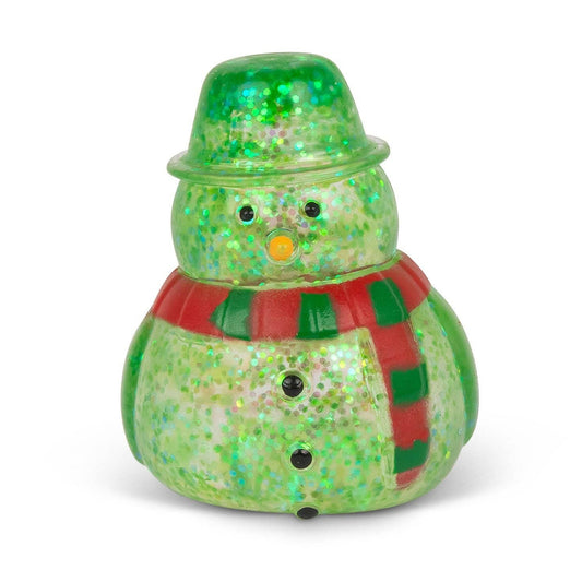 A small snowman figurine with a glittery green body and hat, a red and green striped scarf, and a yellow-orange nose, photographed on a clean white background.