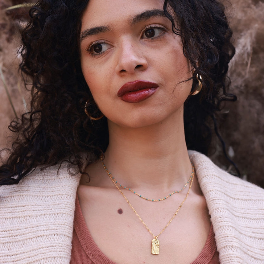 Woman wearing gold necklaces and earrings with a neutral background