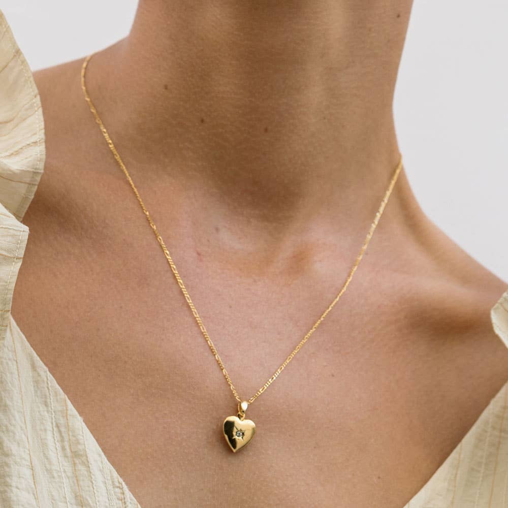 Gold heart-shaped necklace on a person wearing a light-colored top.