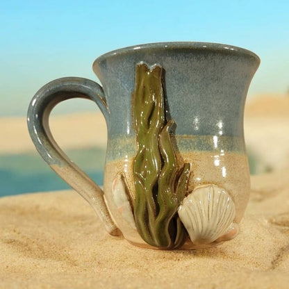 Ceramic mug with ocean-themed design on a sandy surface