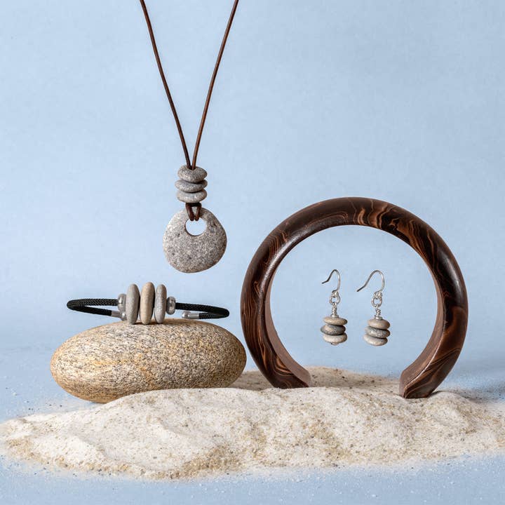 Jewelry set including a necklace, bracelet, and earrings on a sandy surface with a light blue background.