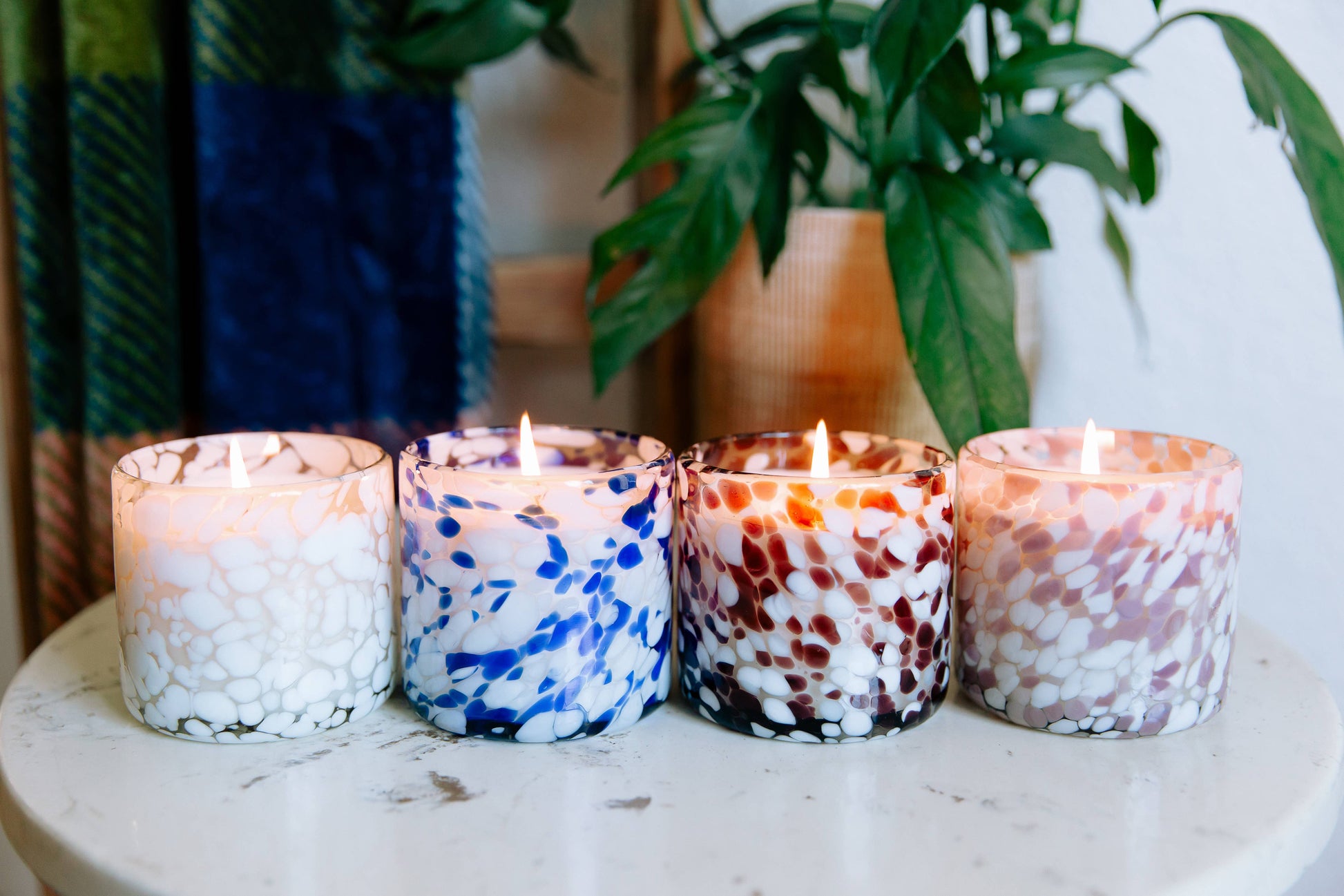 Four colorful candles on a table with plants in the background